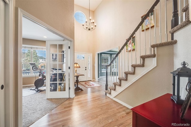 entrance foyer featuring hardwood / wood-style flooring, a towering ceiling, a chandelier, and french doors