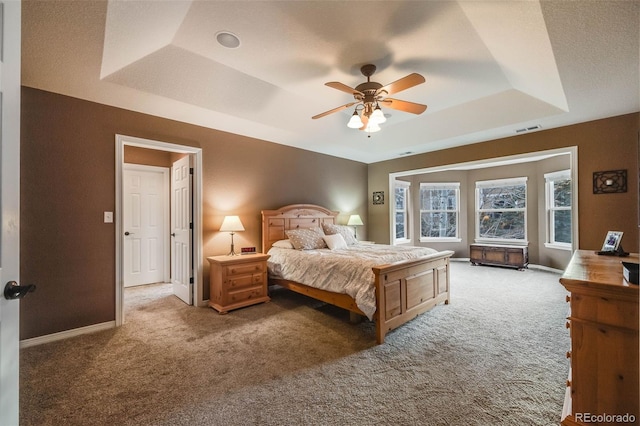 carpeted bedroom with ceiling fan and a raised ceiling