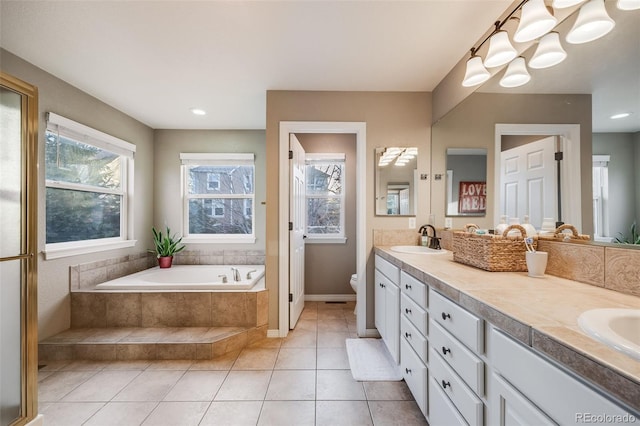 bathroom with tile patterned flooring, vanity, a relaxing tiled tub, and toilet