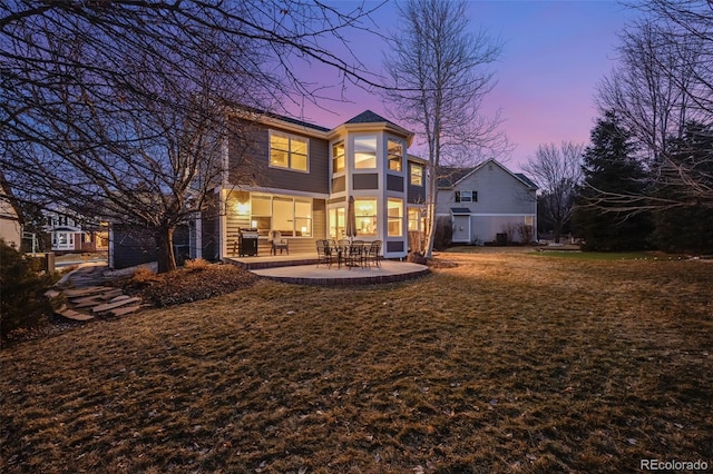 back house at dusk featuring a yard and a patio