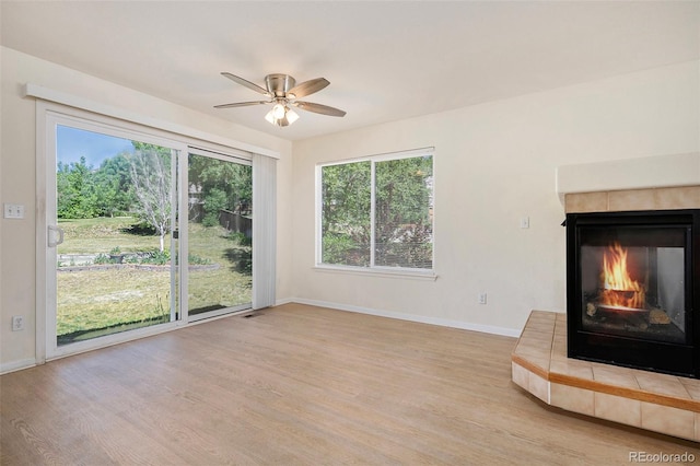 unfurnished living room featuring a ceiling fan, light wood-type flooring, a multi sided fireplace, and baseboards