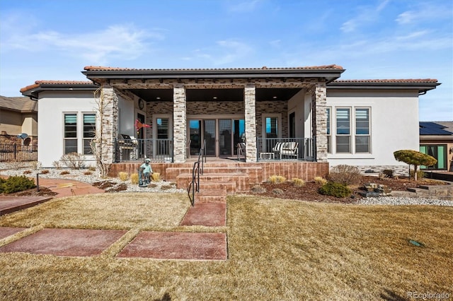 back of house featuring a porch, a tile roof, a lawn, and stucco siding