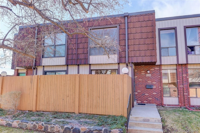 view of side of property with mansard roof, fence, brick siding, and a tiled roof