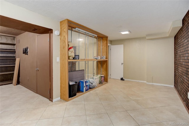 finished basement with tile patterned floors, baseboards, brick wall, and a textured ceiling