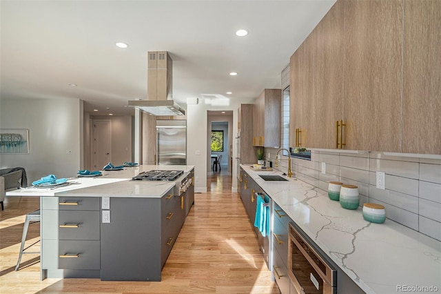 kitchen with appliances with stainless steel finishes, light stone countertops, island range hood, a kitchen island, and light wood-type flooring