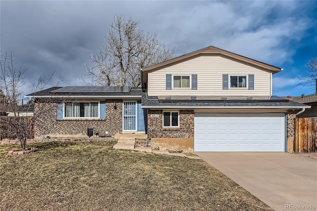 split level home with brick siding, concrete driveway, solar panels, an attached garage, and a front yard