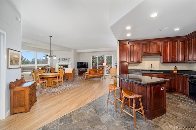 kitchen featuring wood finished floors, a sink, a kitchen breakfast bar, open floor plan, and dark countertops