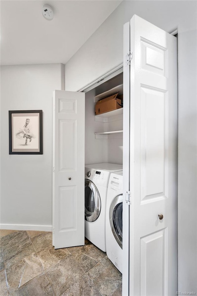 washroom featuring laundry area, stone finish floor, washer and clothes dryer, and baseboards