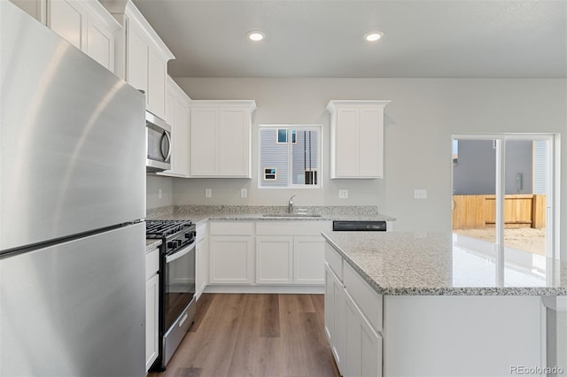 kitchen with light wood finished floors, a kitchen island, recessed lighting, appliances with stainless steel finishes, and a sink