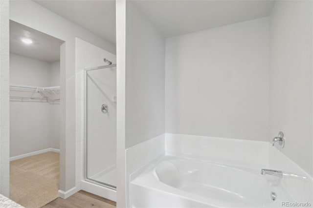 bathroom with wood finished floors, a spacious closet, a bath, and a shower stall