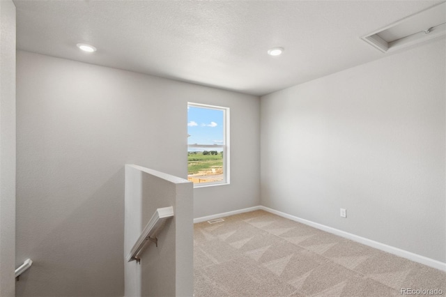 spare room featuring visible vents, baseboards, light colored carpet, and attic access