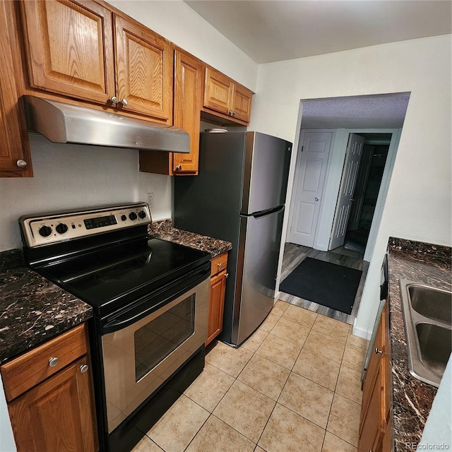 384 S Ironton St Unit 102, Aurora, CO 80012 - kitchen featuring stainless steel appliances, under cabinet range hood, light tile patterned flooring, brown cabinetry, and dark stone counters