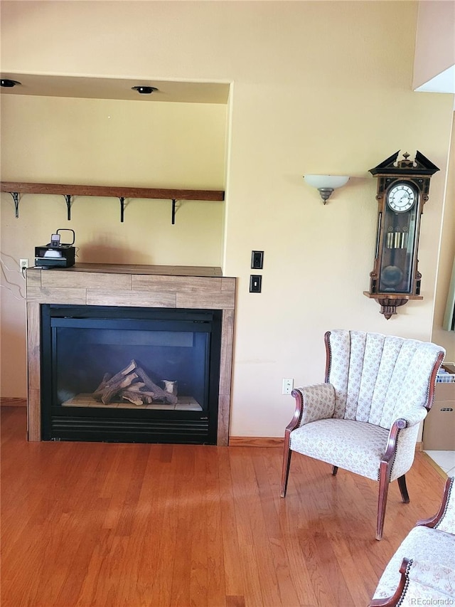 living area with a tile fireplace, baseboards, and wood finished floors