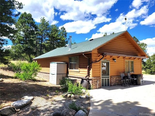 rear view of property featuring a patio, brick siding, and a shingled roof