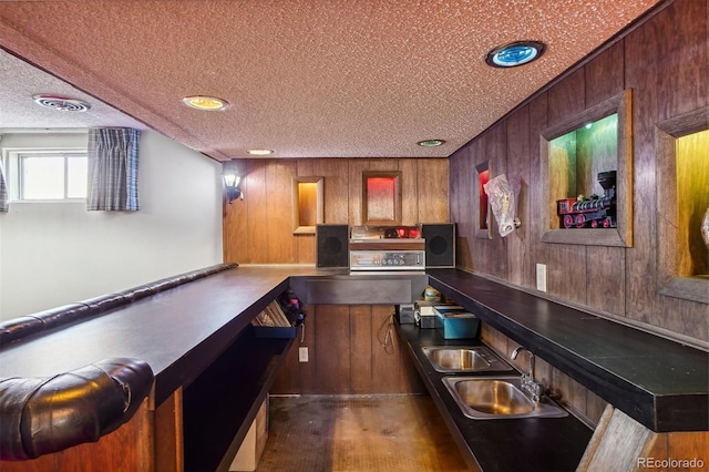 bar featuring a textured ceiling, wooden walls, and sink