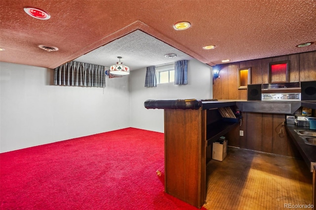 bar featuring sink, hanging light fixtures, a textured ceiling, and dark colored carpet