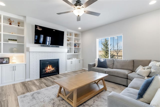 living room with built in shelves, a ceiling fan, recessed lighting, light wood finished floors, and a brick fireplace