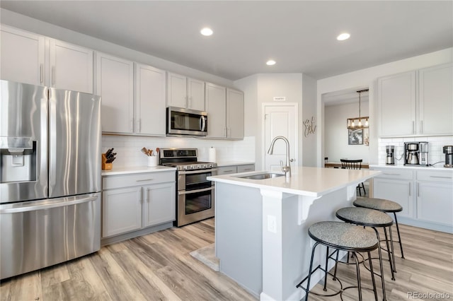 kitchen featuring light wood-style flooring, a sink, appliances with stainless steel finishes, a breakfast bar area, and light countertops