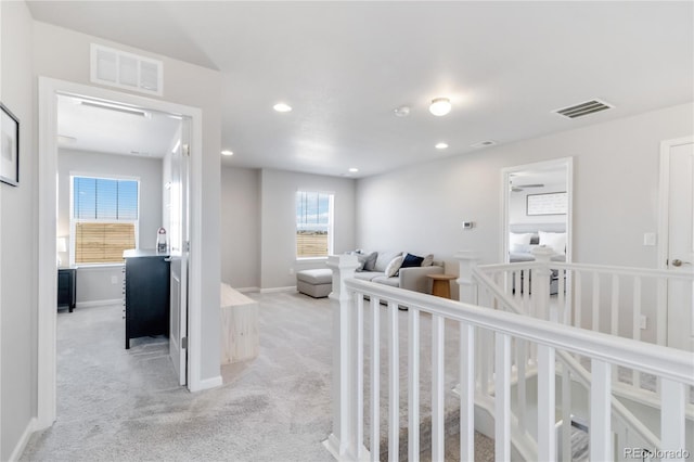 hallway with visible vents, an upstairs landing, light colored carpet, and baseboards