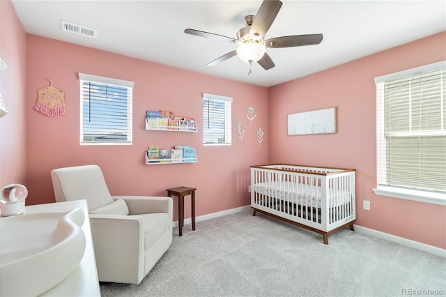 carpeted bedroom with visible vents, a crib, baseboards, and a ceiling fan