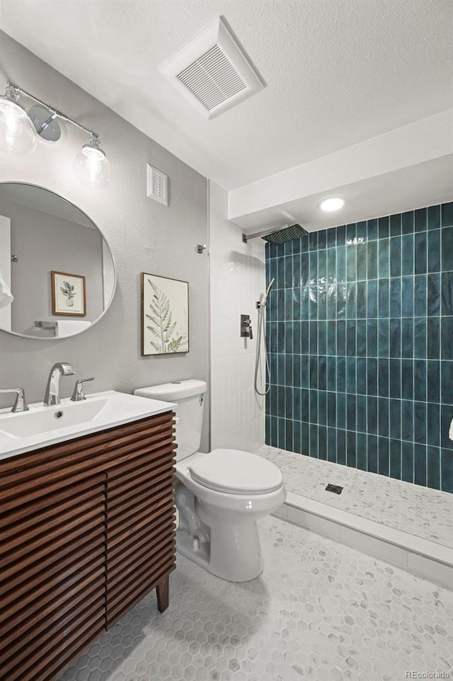 bathroom with a textured ceiling, visible vents, a tile shower, vanity, and toilet