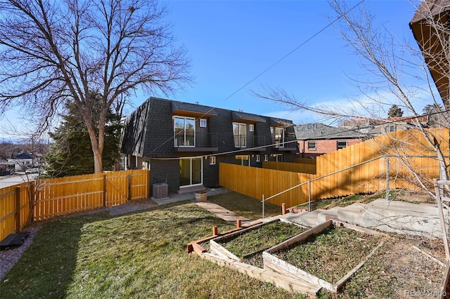 rear view of property featuring a lawn, a fenced backyard, central AC, and a vegetable garden