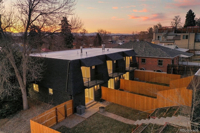 back of property at dusk featuring roof with shingles, fence, cooling unit, and a balcony