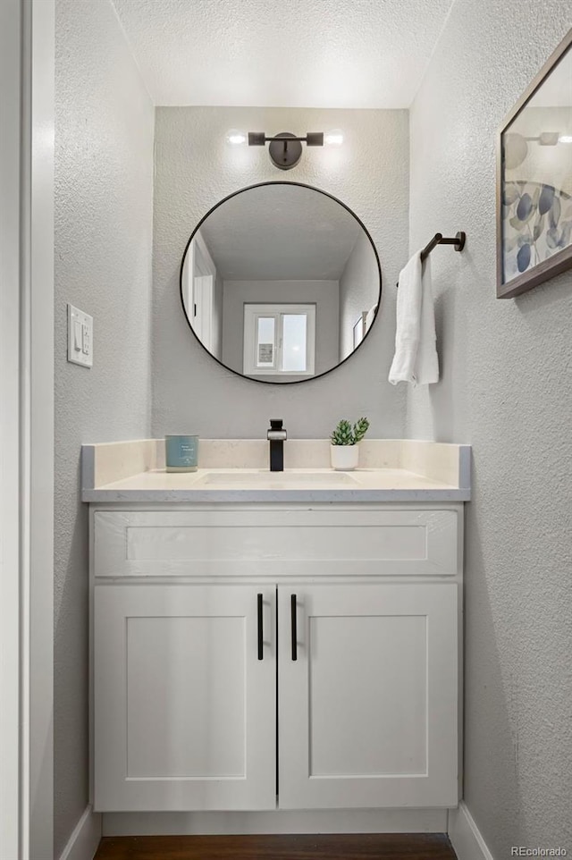bathroom with a textured ceiling, a textured wall, baseboards, and vanity