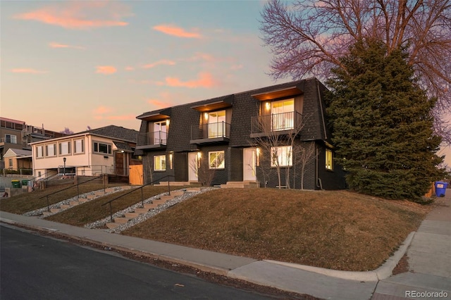 view of front of house with fence, mansard roof, brick siding, and a balcony