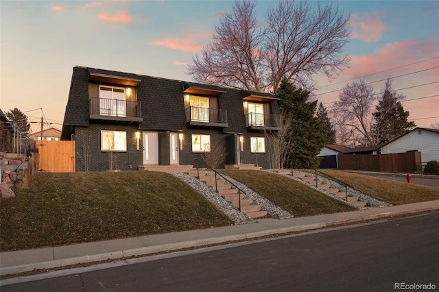 modern home featuring fence, a lawn, mansard roof, and a balcony