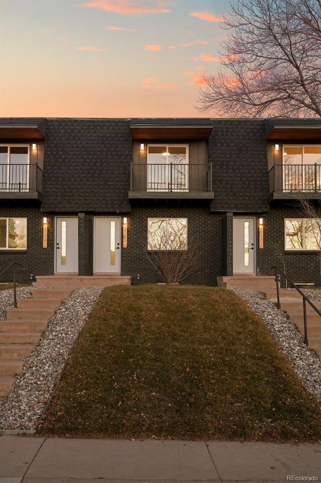 view of front of house with a shingled roof, brick siding, and a balcony