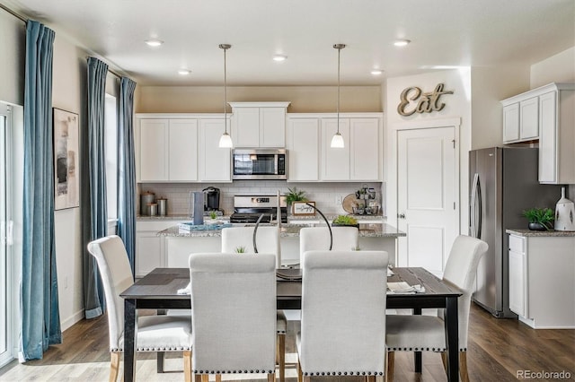 kitchen with wood finished floors, appliances with stainless steel finishes, backsplash, and a kitchen island with sink