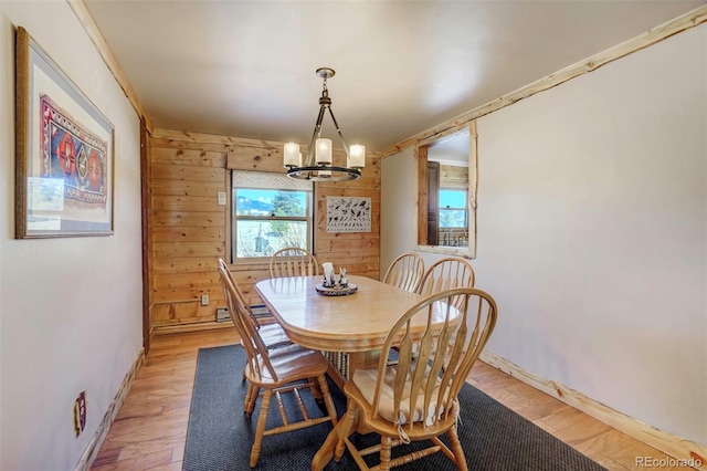 dining area featuring light wood-type flooring, wooden walls, and an inviting chandelier