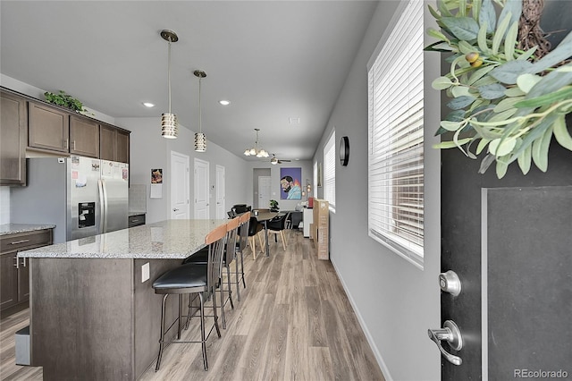 847 Great Plains Ave, Berthoud, CO 80513 - kitchen featuring stainless steel fridge with ice dispenser, light wood finished floors, dark brown cabinetry, a kitchen bar, and light stone countertops