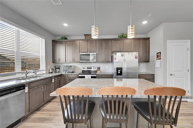 847 Great Plains Ave, Berthoud, CO 80513 - kitchen featuring appliances with stainless steel finishes, light wood-style flooring, a kitchen island, light stone counters, and dark brown cabinets