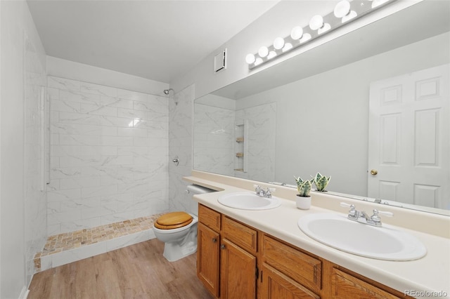 bathroom with tiled shower, toilet, vanity, and hardwood / wood-style flooring