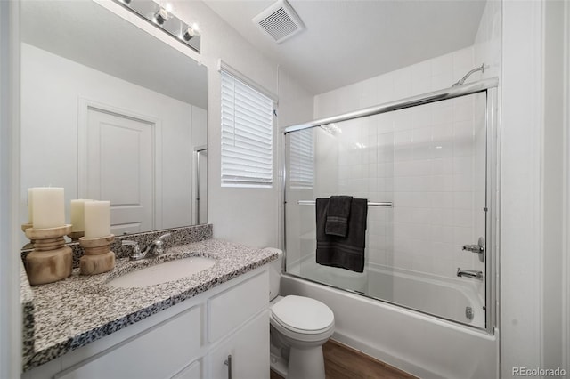 46558 Avery Ln, Bennett, CO 80102 - full bathroom featuring bath / shower combo with glass door, toilet, visible vents, vanity, and wood finished floors