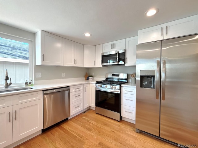 kitchen with appliances with stainless steel finishes, sink, white cabinets, and light wood-type flooring