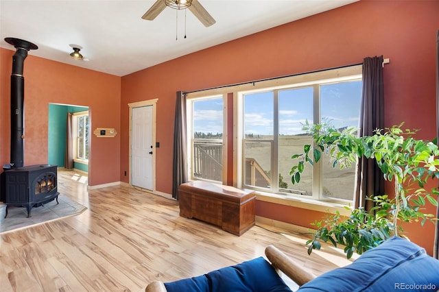 living room with light hardwood / wood-style flooring, a wood stove, and ceiling fan