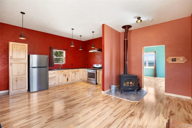 kitchen with decorative light fixtures, light hardwood / wood-style floors, appliances with stainless steel finishes, and a wood stove