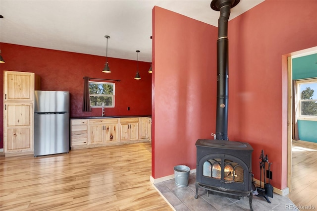 kitchen featuring hardwood / wood-style flooring, a wood stove, pendant lighting, and stainless steel fridge