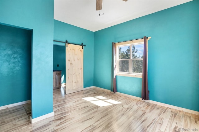 unfurnished bedroom with ceiling fan, light hardwood / wood-style flooring, and a barn door