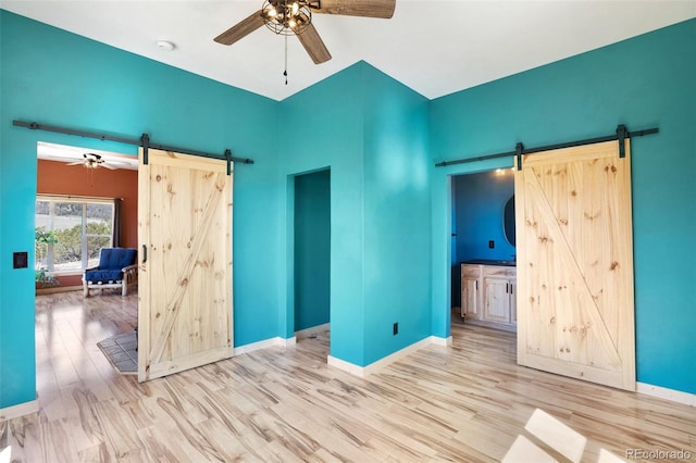 unfurnished bedroom with wood-type flooring, ceiling fan, ensuite bathroom, and a barn door