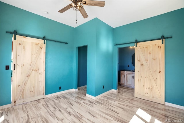 unfurnished bedroom with ceiling fan, hardwood / wood-style flooring, connected bathroom, and a barn door