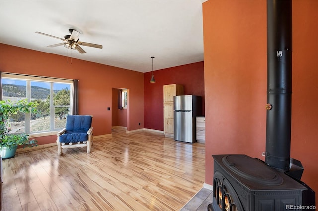 sitting room with hardwood / wood-style floors, ceiling fan, and a wood stove