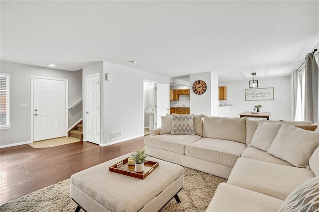 living area featuring wood-type flooring, visible vents, baseboards, and stairs