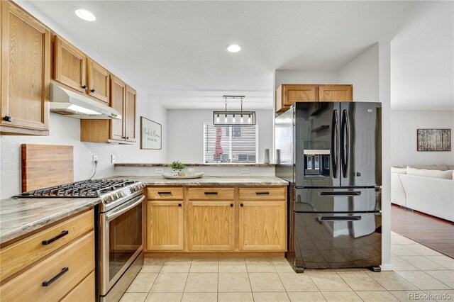 kitchen with under cabinet range hood, stainless steel range with gas stovetop, black fridge, and light tile patterned flooring