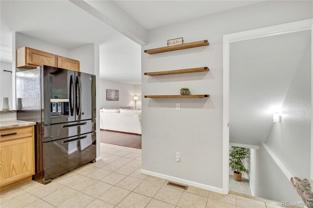 kitchen with light tile patterned floors, light brown cabinets, black fridge with ice dispenser, visible vents, and light countertops