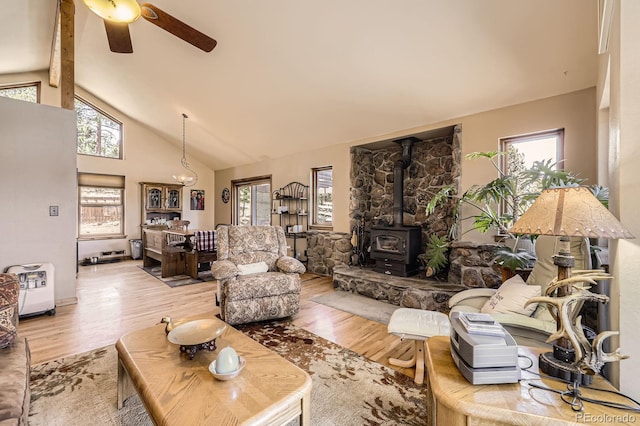 living area with ceiling fan, beamed ceiling, high vaulted ceiling, a wood stove, and wood finished floors