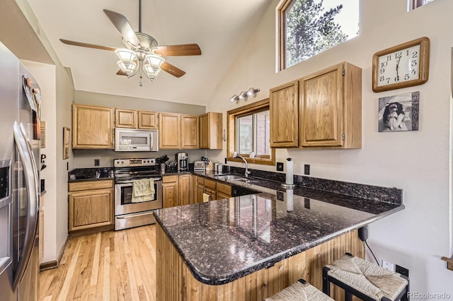 kitchen featuring a peninsula, a ceiling fan, dark stone countertops, a sink, and stainless steel appliances